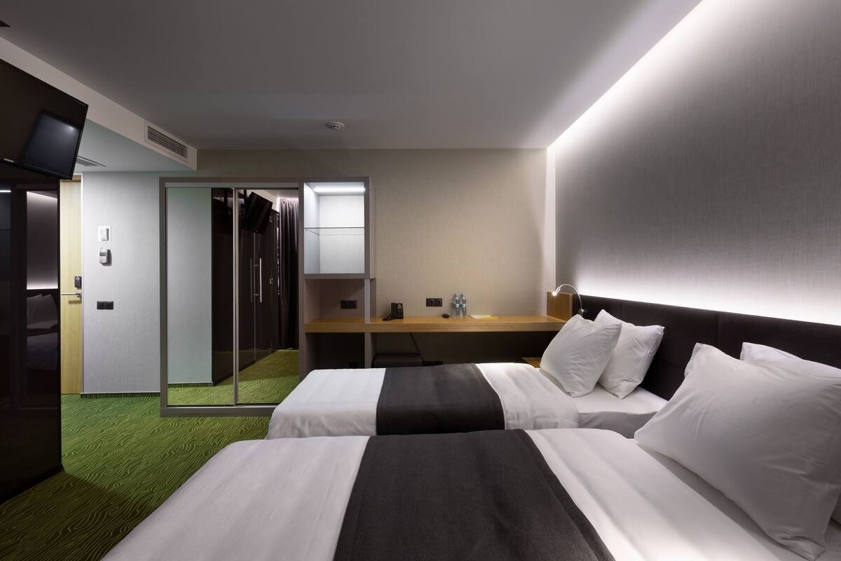 A hotel room with two beds, a desk, a mirror, and a television.