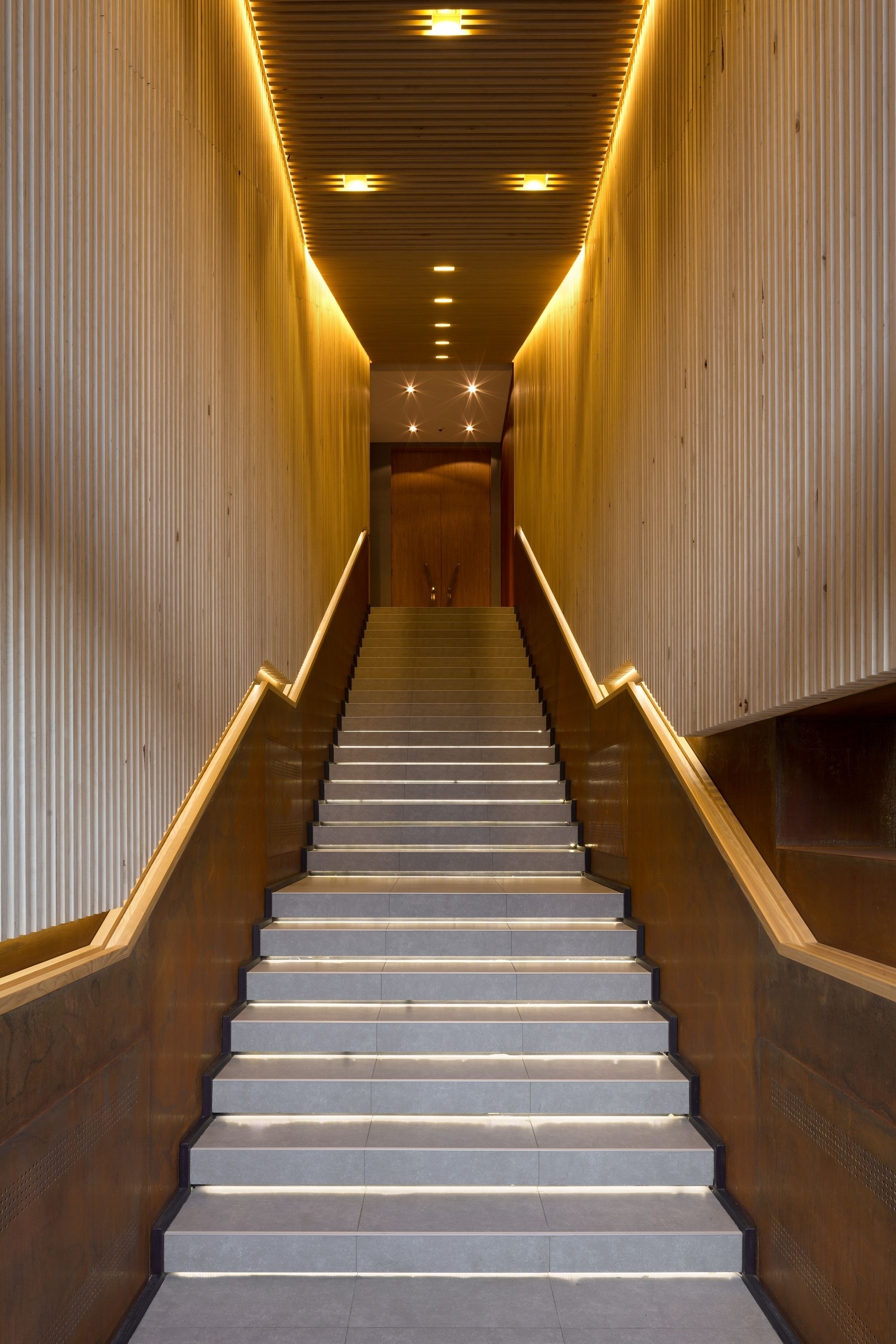 Una escalera con barandilla de madera e iluminación en ambos lados.