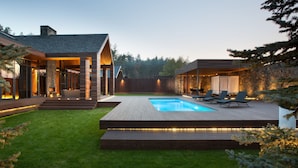 Una casa moderna con piscina, terrazza in legno e area salotto esterna.