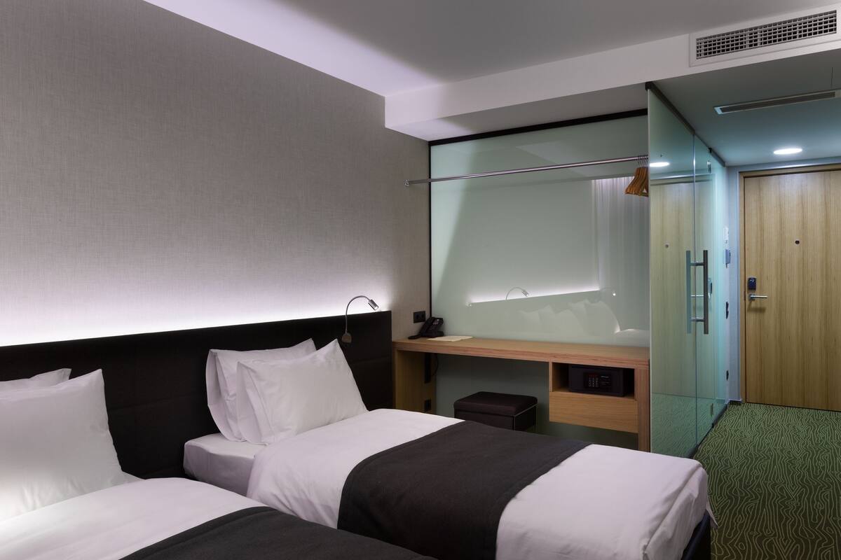 A hotel room with two beds, a desk, a mirror, a wardrobe, and a small seating area.