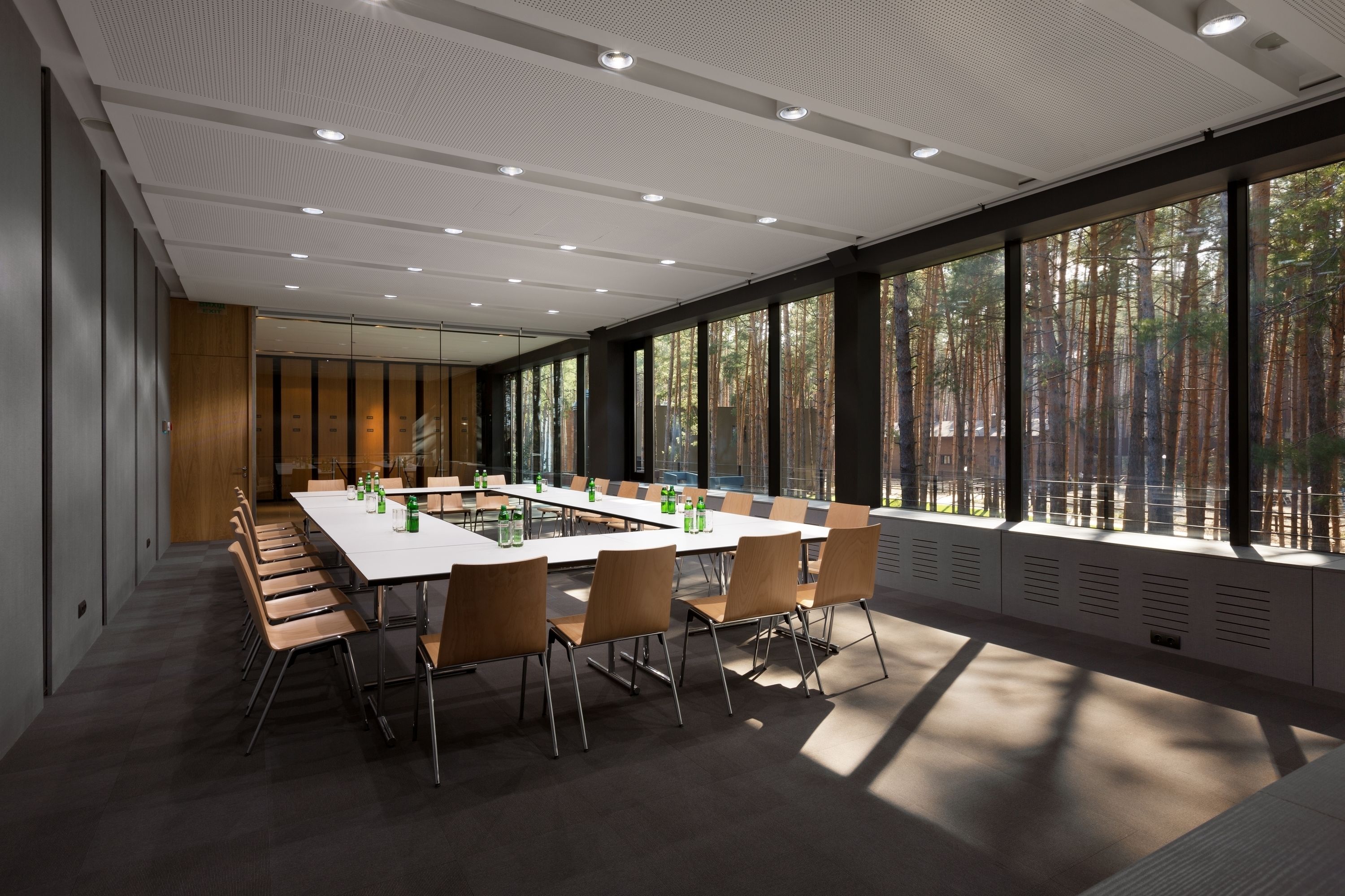 A conference room with a long table, chairs, and large windows with a forest view.