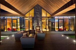 Um interior moderno com lareira central, soalho de madeira e portas de vidro que dão para os quartos.