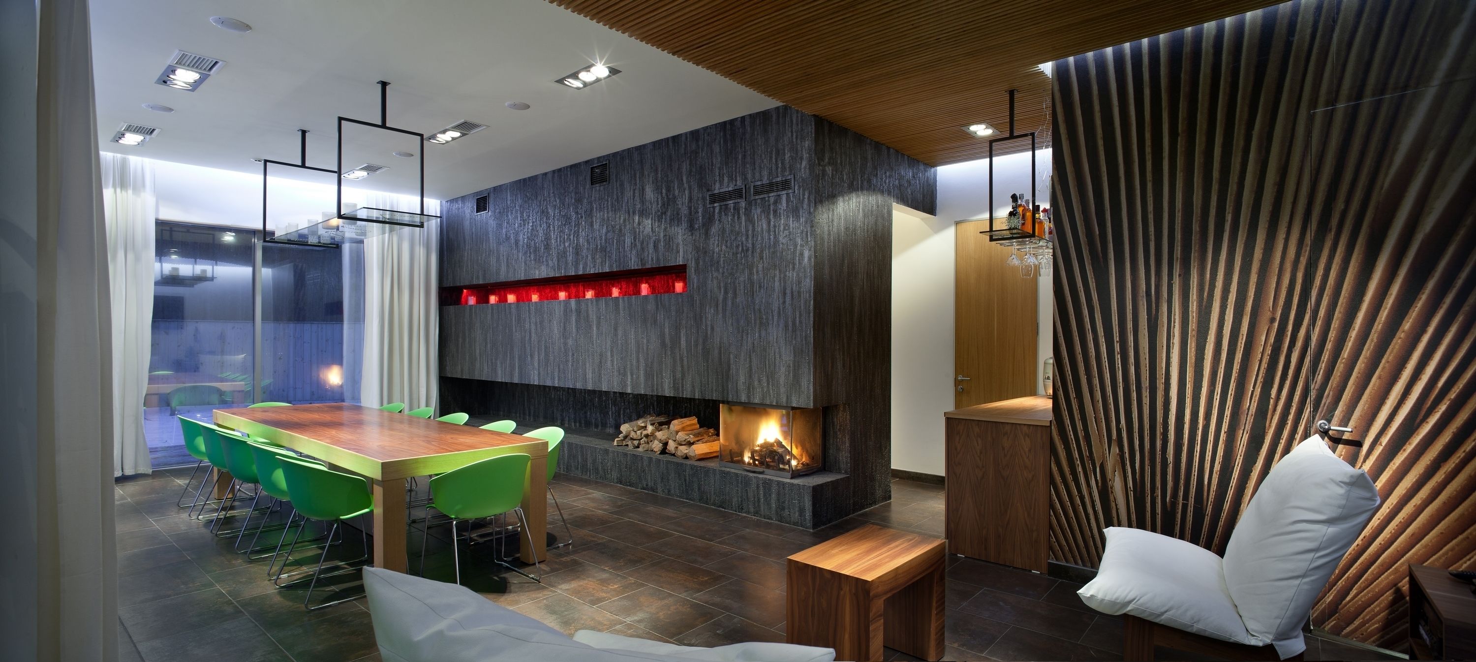 A modern dining area with a wooden table and green chairs, a fireplace, and a view of the outdoors.