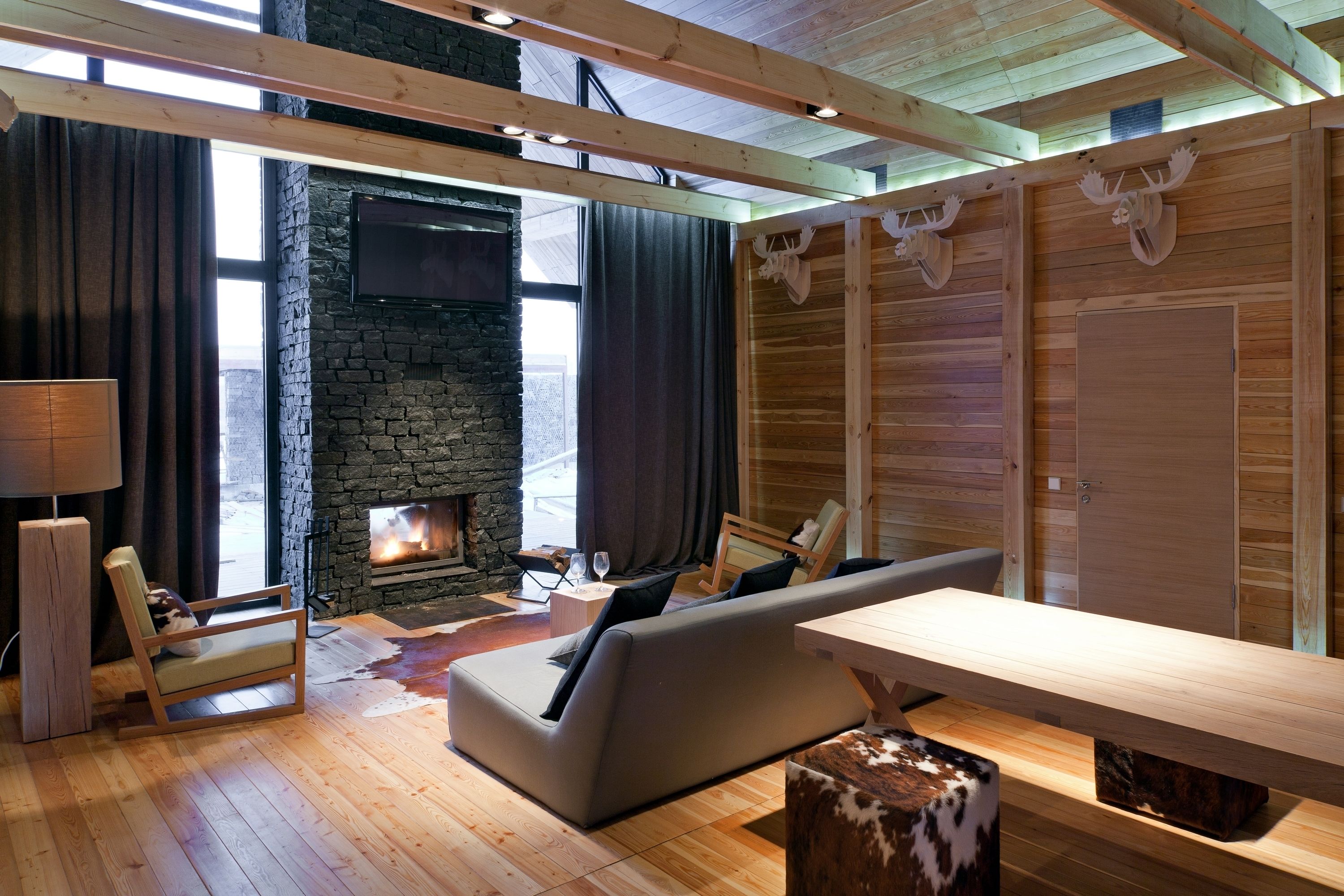A cozy living room with a stone fireplace, wooden beams, and a large window.