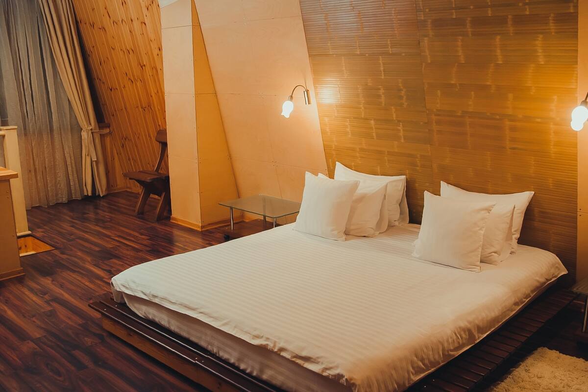 A neatly made bed with white linens in a room with wooden flooring and a sloped ceiling.