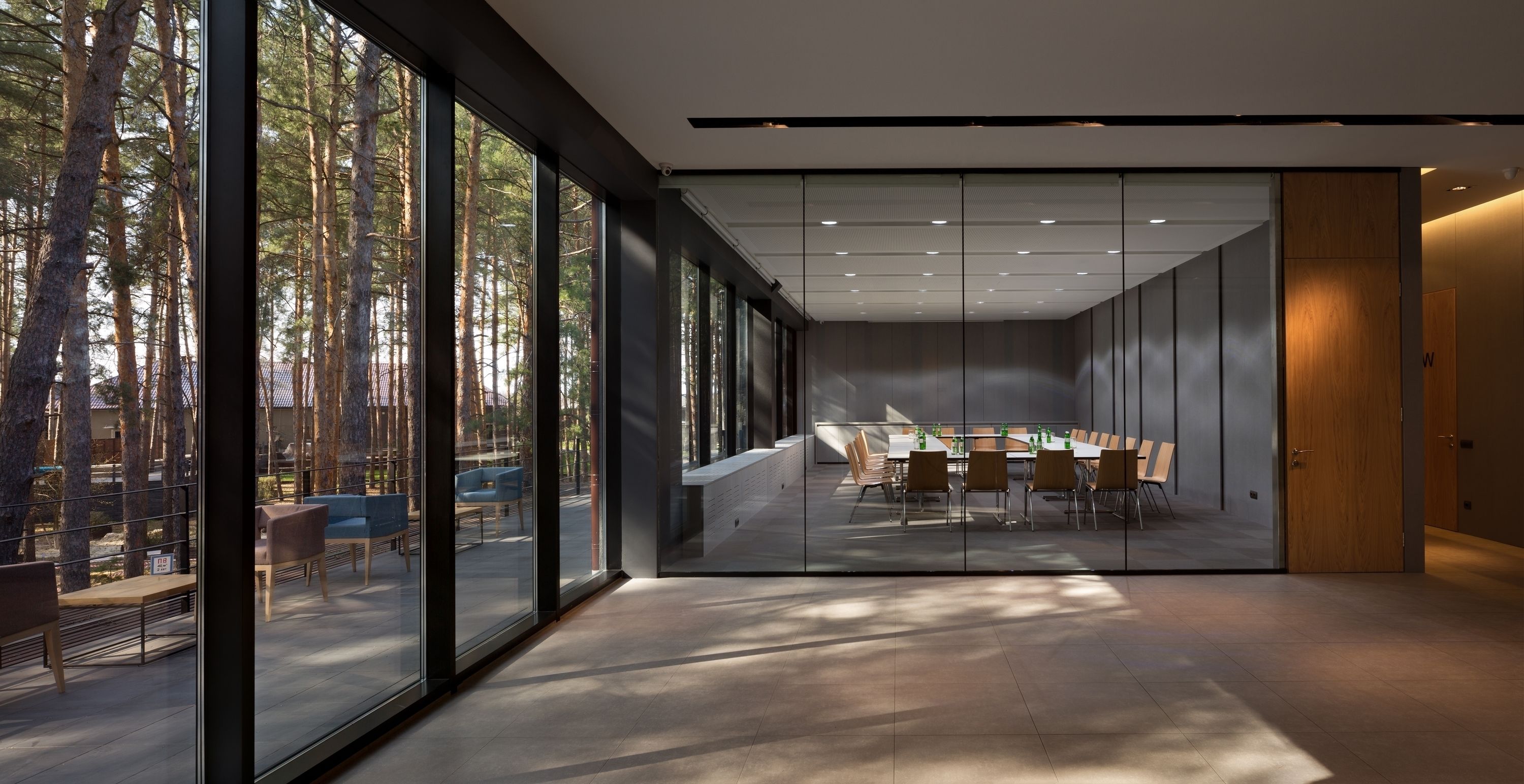 A modern conference room with a glass partition, large windows, and a view of a forest.