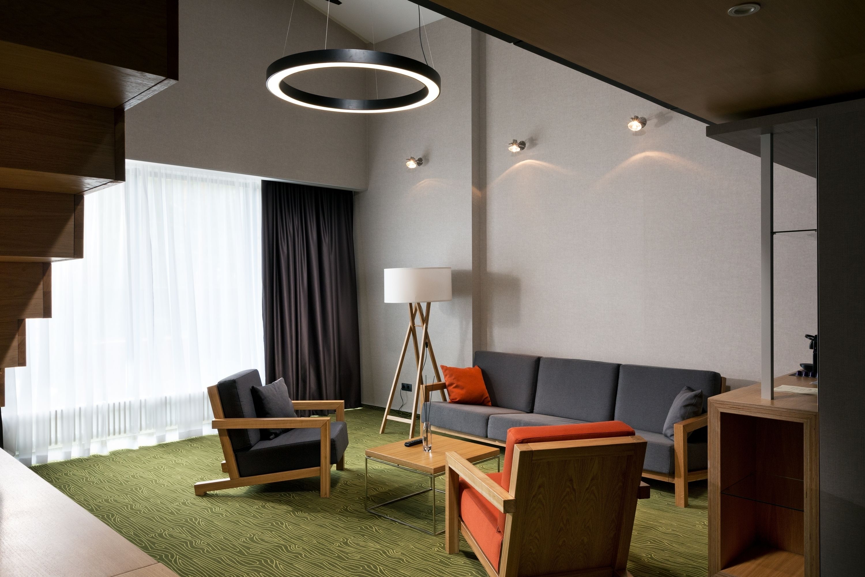 A modern hotel room with a sofa, two armchairs, a coffee table, and a floor lamp.