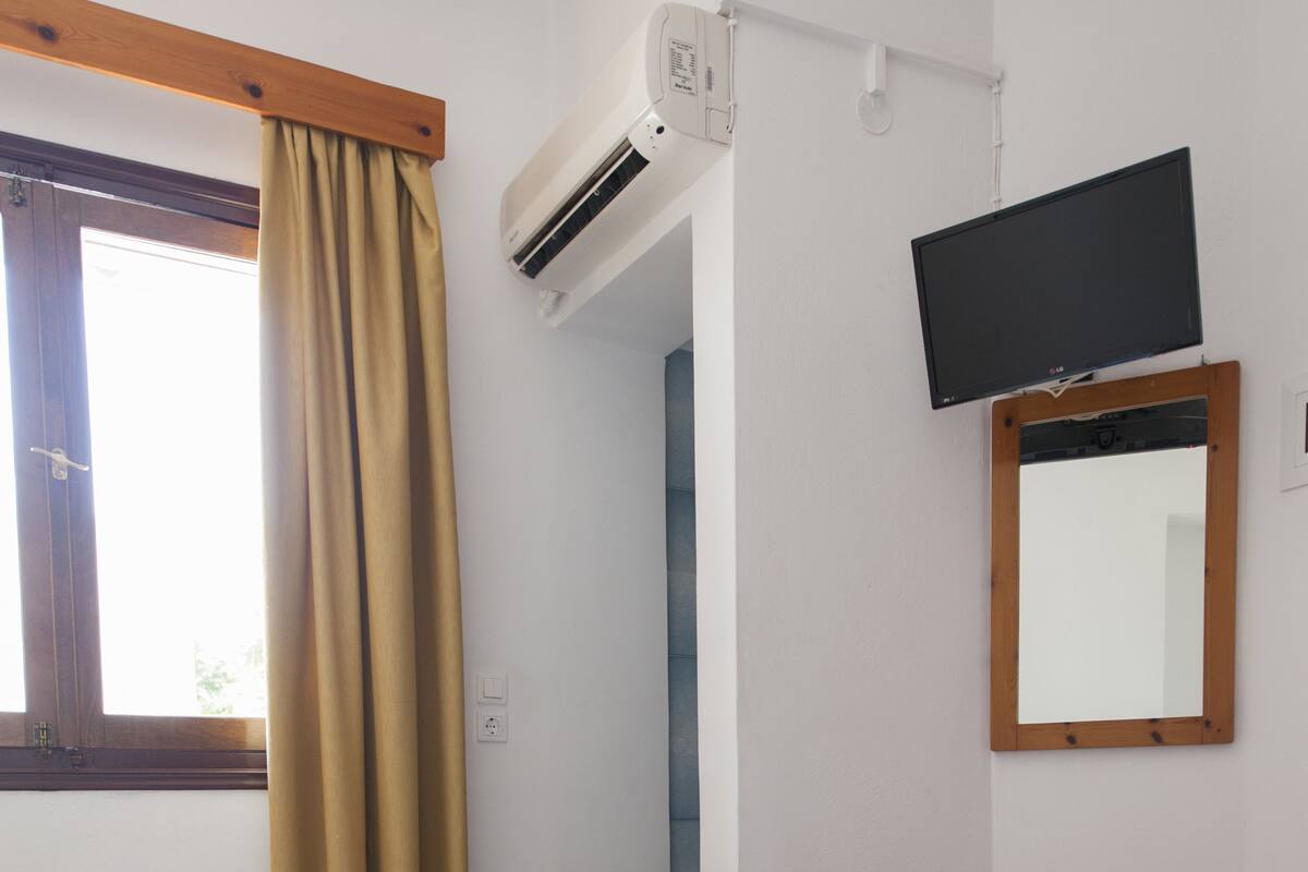 A hotel room with two beds, an air conditioning unit, a television, a mirror, and a small wooden table.