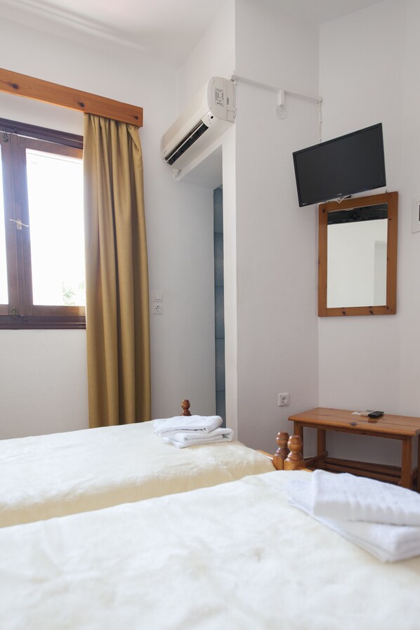 Habitación de hotel con dos camas, un equipo de aire acondicionado, un televisor, un espejo y una pequeña mesa de madera.