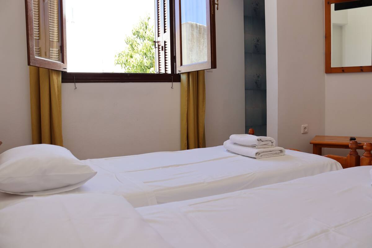 A hotel room with two beds, a wooden nightstand, a mirror, and a window with curtains.