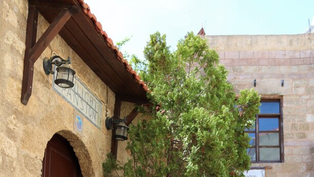 A narrow cobblestone street with a stone building featuring a large wooden door and a sign reading "PANSTON." - Stavros Pension (Rhodes)