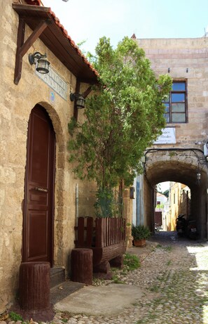 A narrow cobblestone street with a stone building featuring a large wooden door and a sign reading "PANSTON." - Stavros Pension (Rhodes)