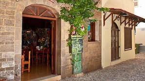 A stone building with an open doorway leading to a dining area. A chalkboard sign is visible on the wall. - Stavros Pension (Rhodes)