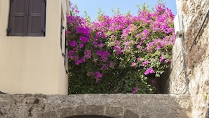 A stone archway in a narrow street, with a building on the left and a wall on the right. - Stavros Pension (Rhodes)