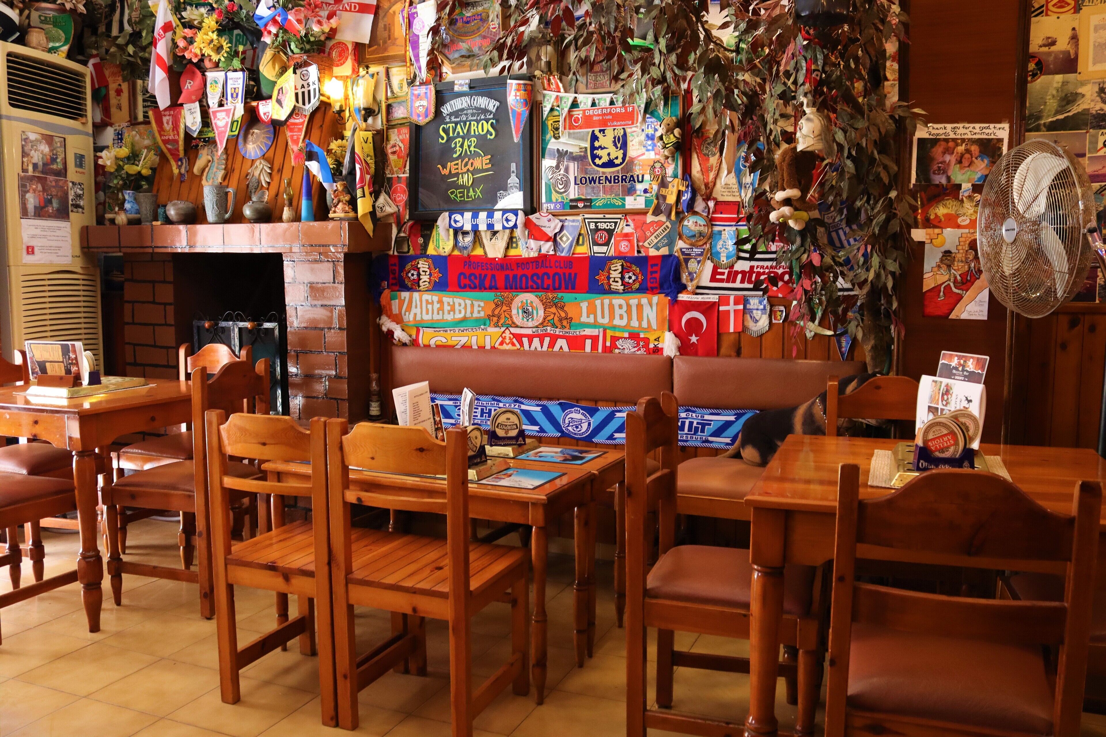 A restaurant with wooden tables and chairs, a brick fireplace, and various decorations including flags and signs.