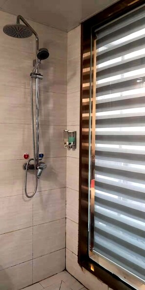 Une douche équipée d’un pommeau de douche et d’un flexible à main, d’un panneau de commande avec des boutons et d’une fenêtre avec des stores horizontaux.