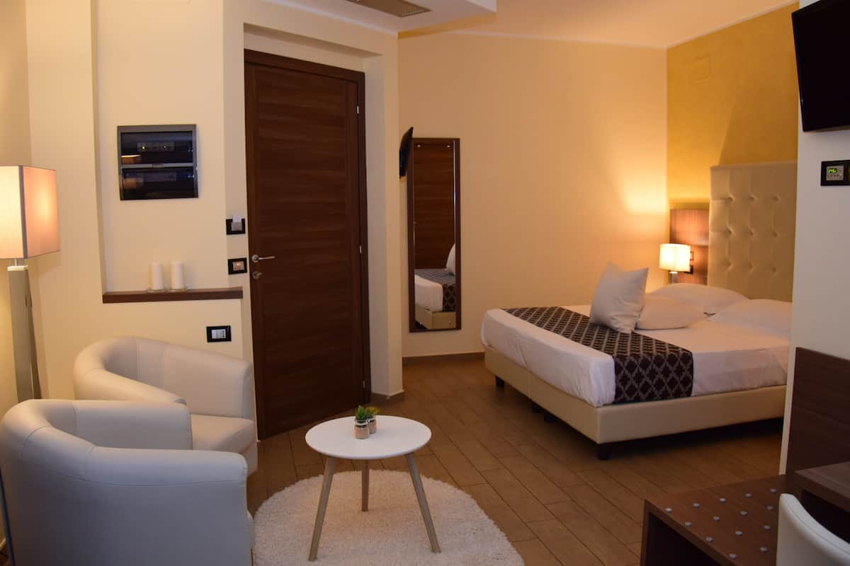 Une chambre d’hôtel avec un lit, une chaise, une petite table avec une plante, un miroir et une porte.