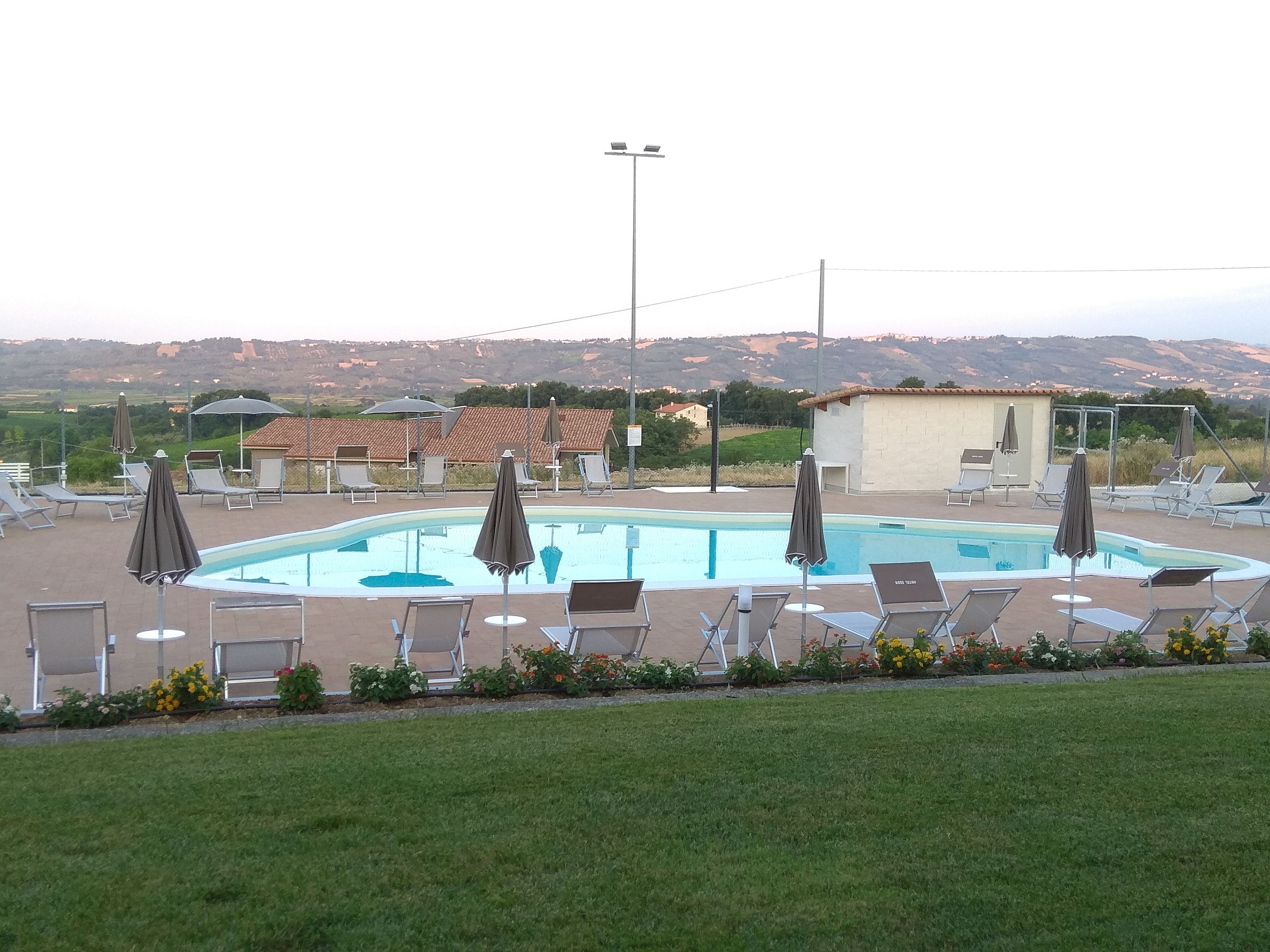 A swimming pool with lounge chairs and umbrellas, surrounded by a grassy area and buildings in the background.
