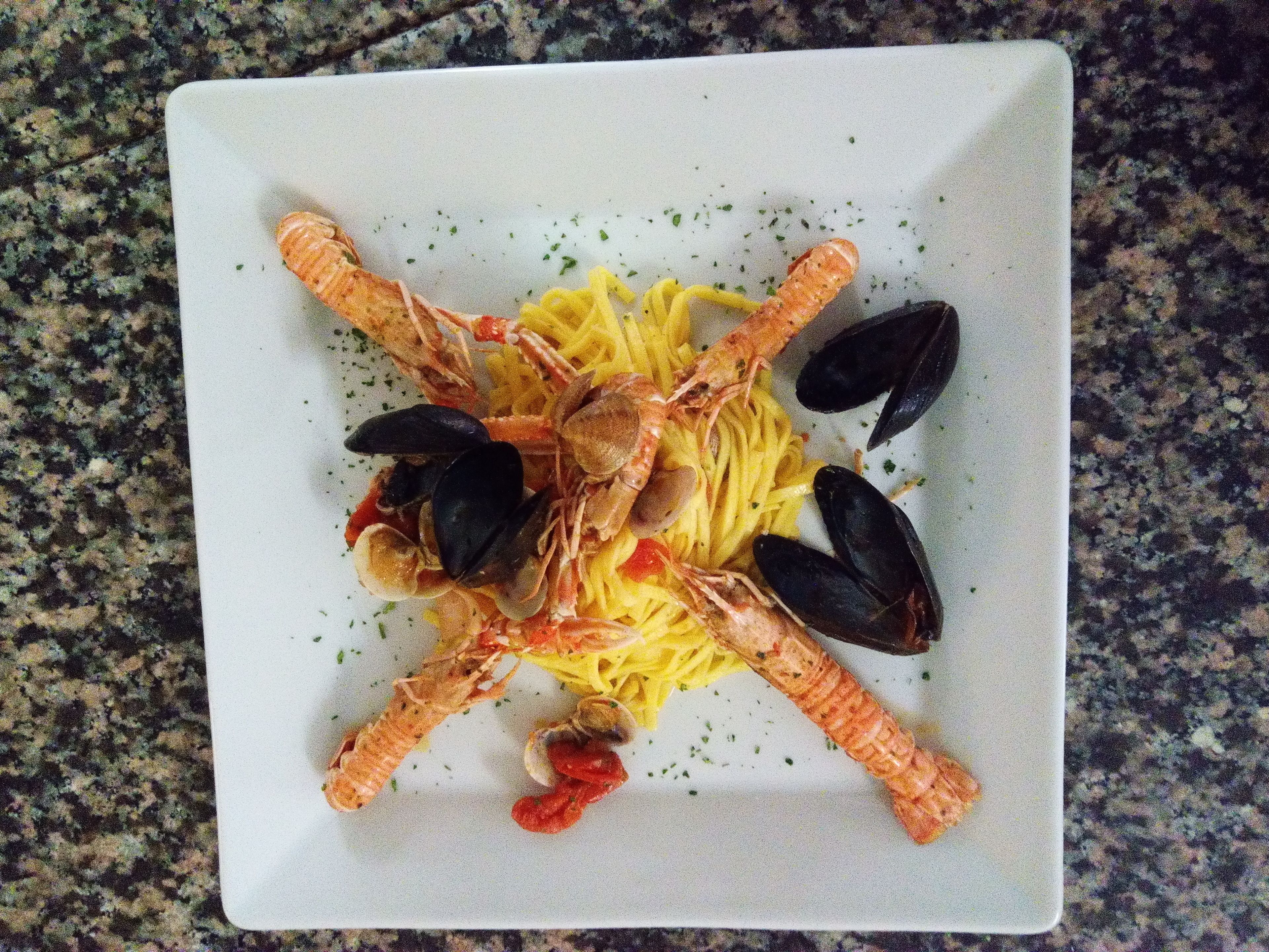 A square plate with pasta, mussels, and shrimp arranged in a cross pattern.
