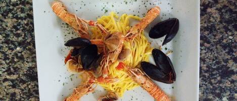 En fyrkantig tallrik med pasta, musslor och räkor, arrangerade i ett korsmönster.