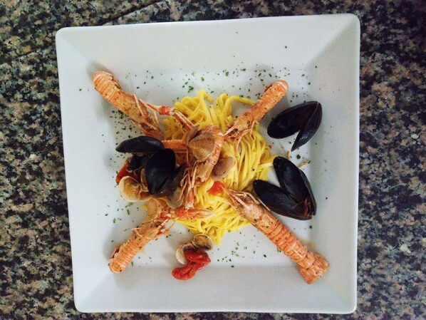 A square plate with pasta, mussels, and shrimp arranged in a cross pattern. - Hotel Residence Eden (Mozzagrogna)