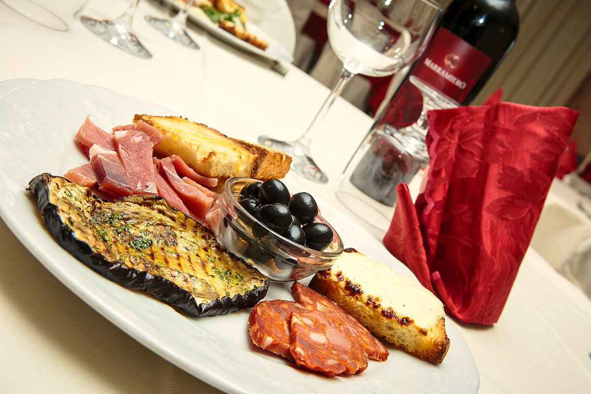A plate of food with grilled eggplant, ham, cheese, and olives.