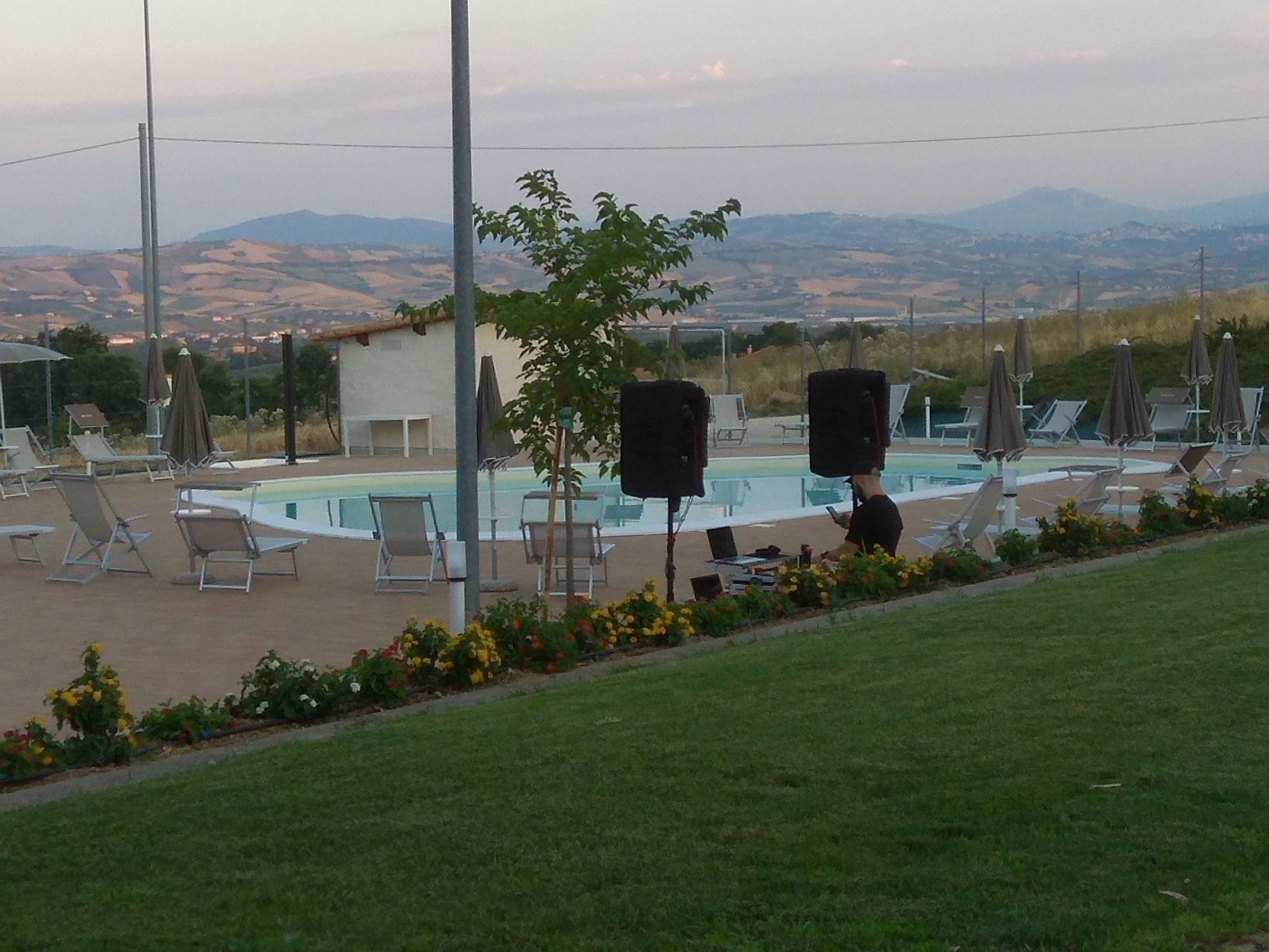 Un área de piscina con sillas de descanso y sombrillas, rodeada de césped y montañas al fondo.