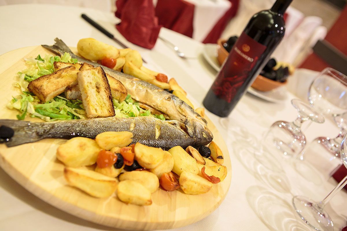 Una tabla de madera con pescado a la parrilla, pan tostado y patatas asadas.