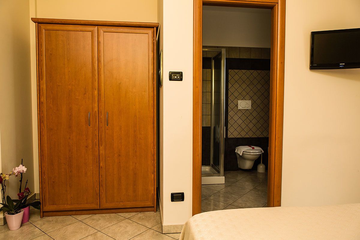 Een hotelkamer met een houten kledingkast, een bed, een aan de muur bevestigde televisie en een badkamer die door een open deur zichtbaar is.