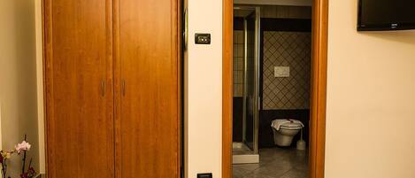 A hotel room with a wooden wardrobe, a bed, a television mounted on the wall, and a bathroom visible through an open door.