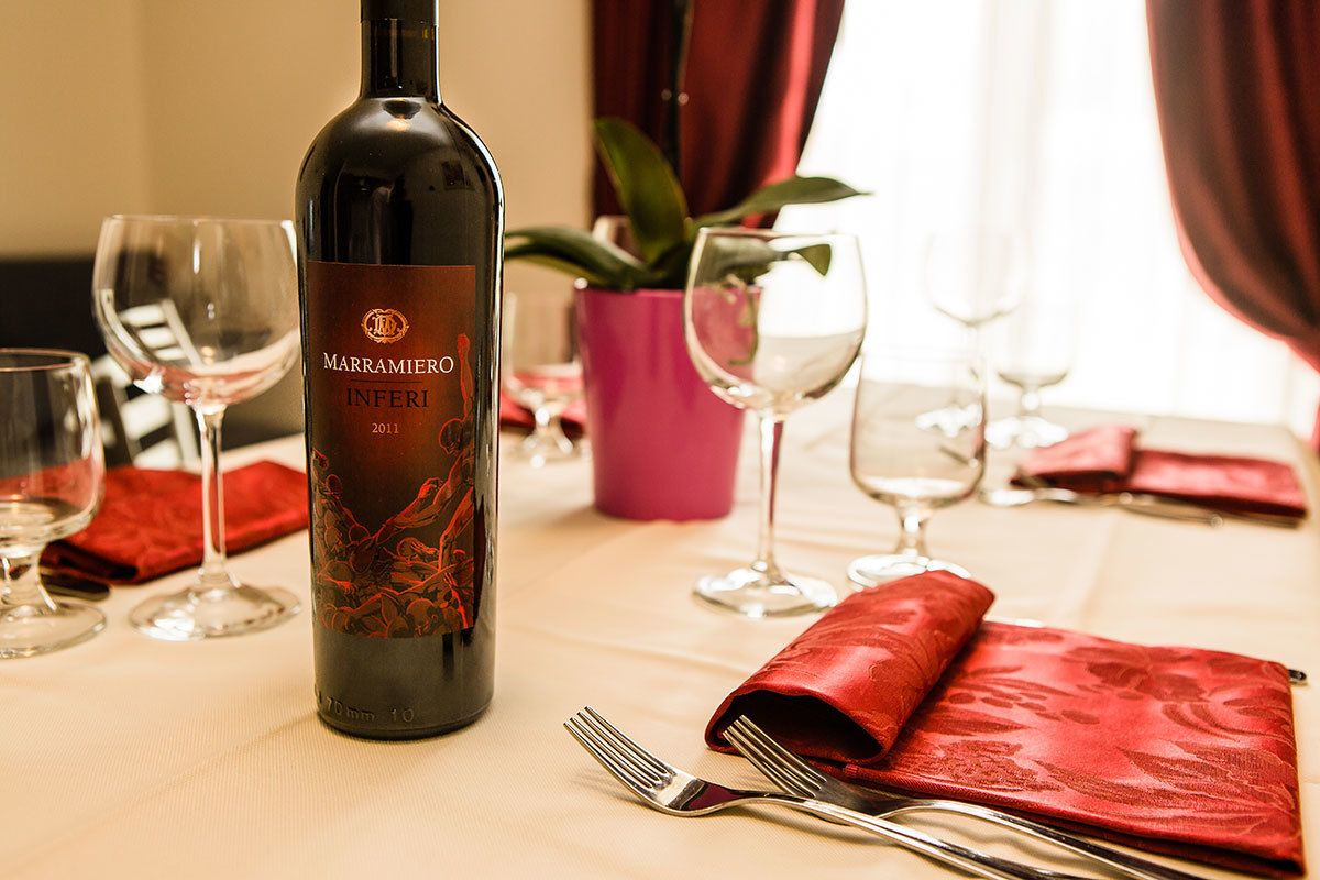 A bottle of wine, a fork, and a knife on a table with a red napkin and a potted plant in the background.