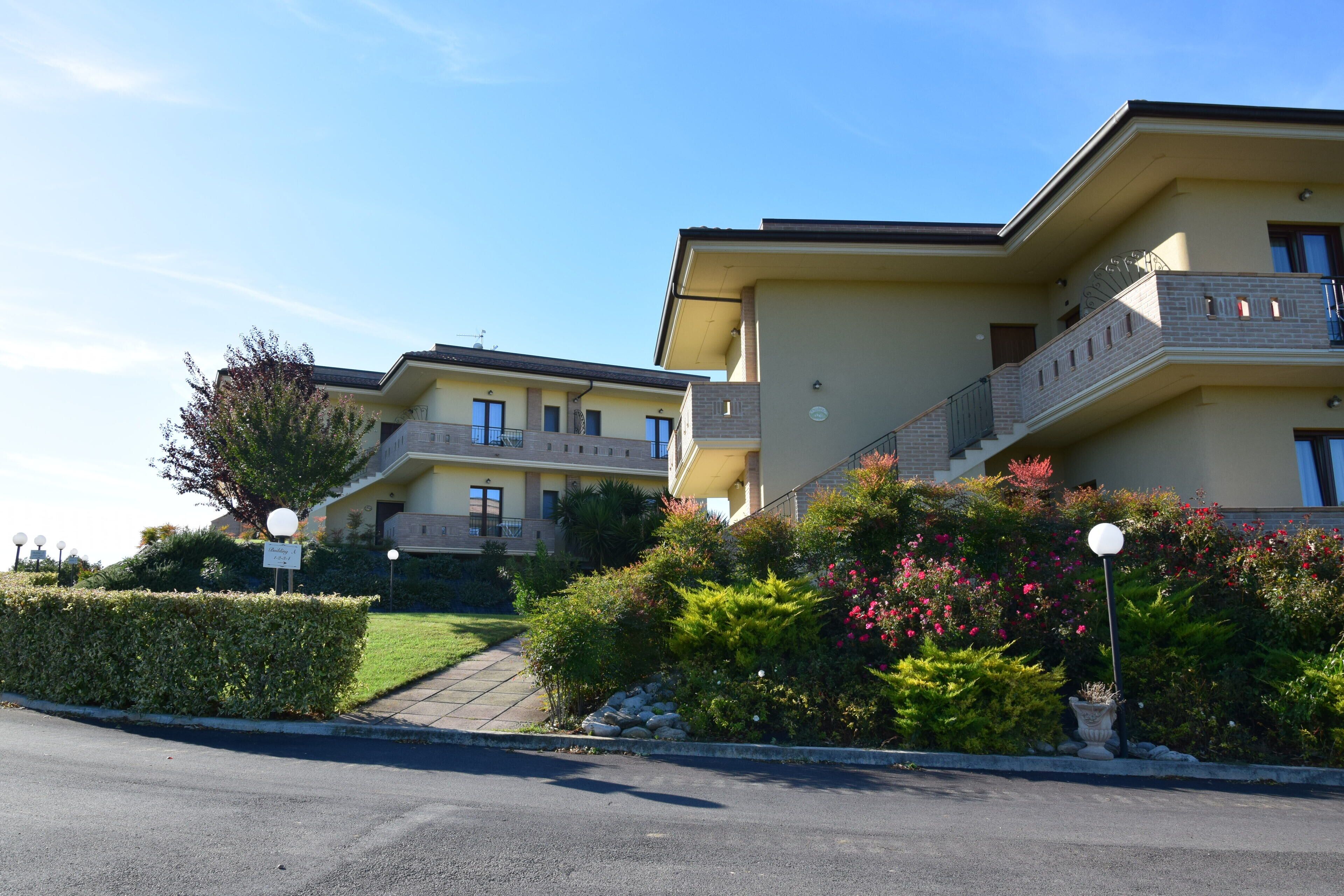 A multi-story residential building with balconies, a paved driveway, and landscaped gardens.