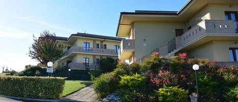 A multi-story residential building with balconies, a paved driveway, and landscaped gardens.