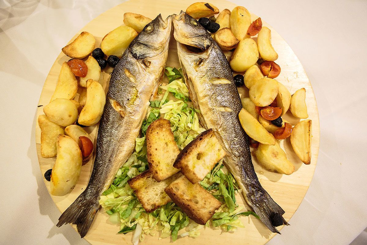 A wooden platter with two whole fish, roasted potatoes, and some greens.
