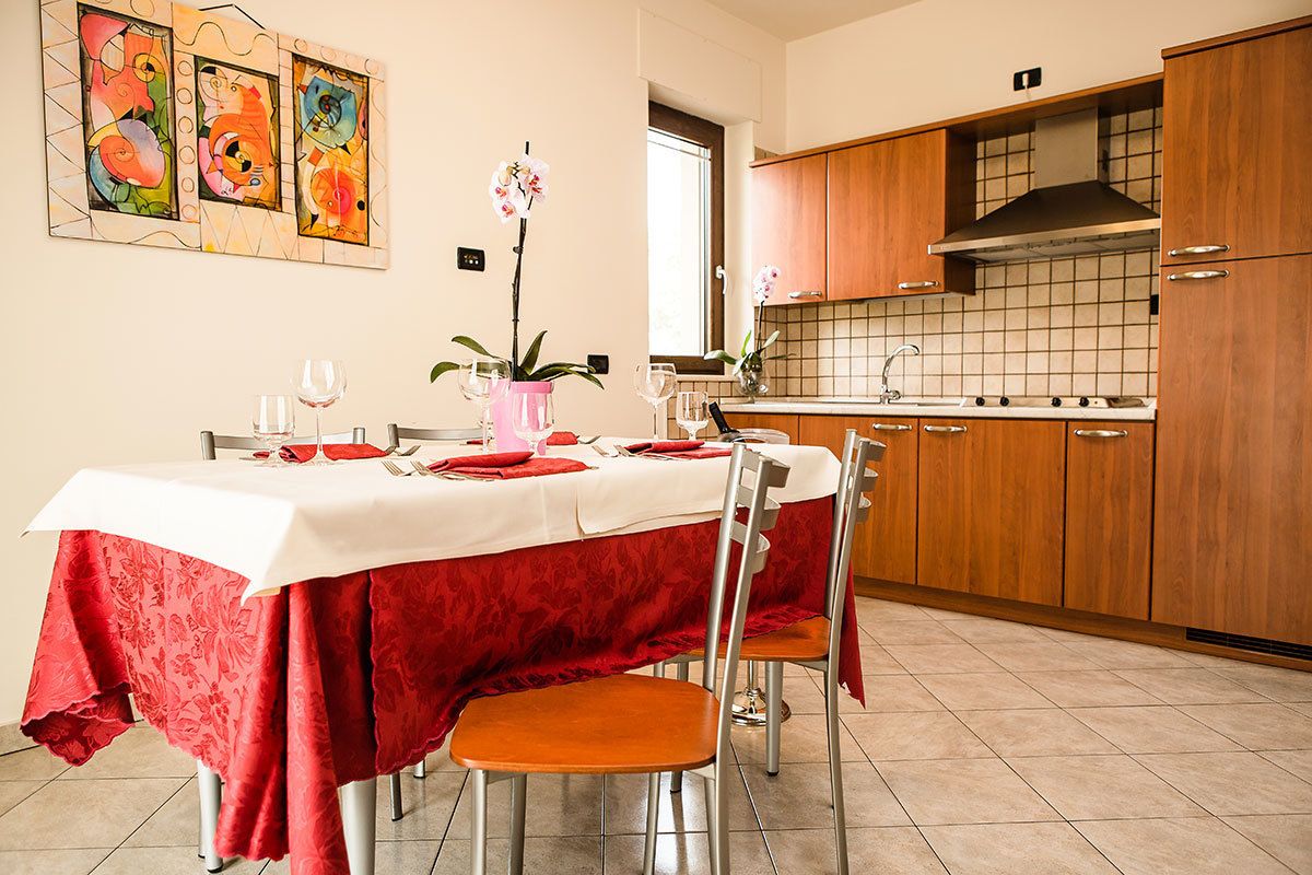 A dining area with a table set for four, a kitchen in the background, and a window with natural light.