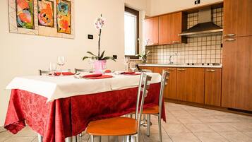 A dining area with a table set for four, a kitchen in the background, and a window with natural light.