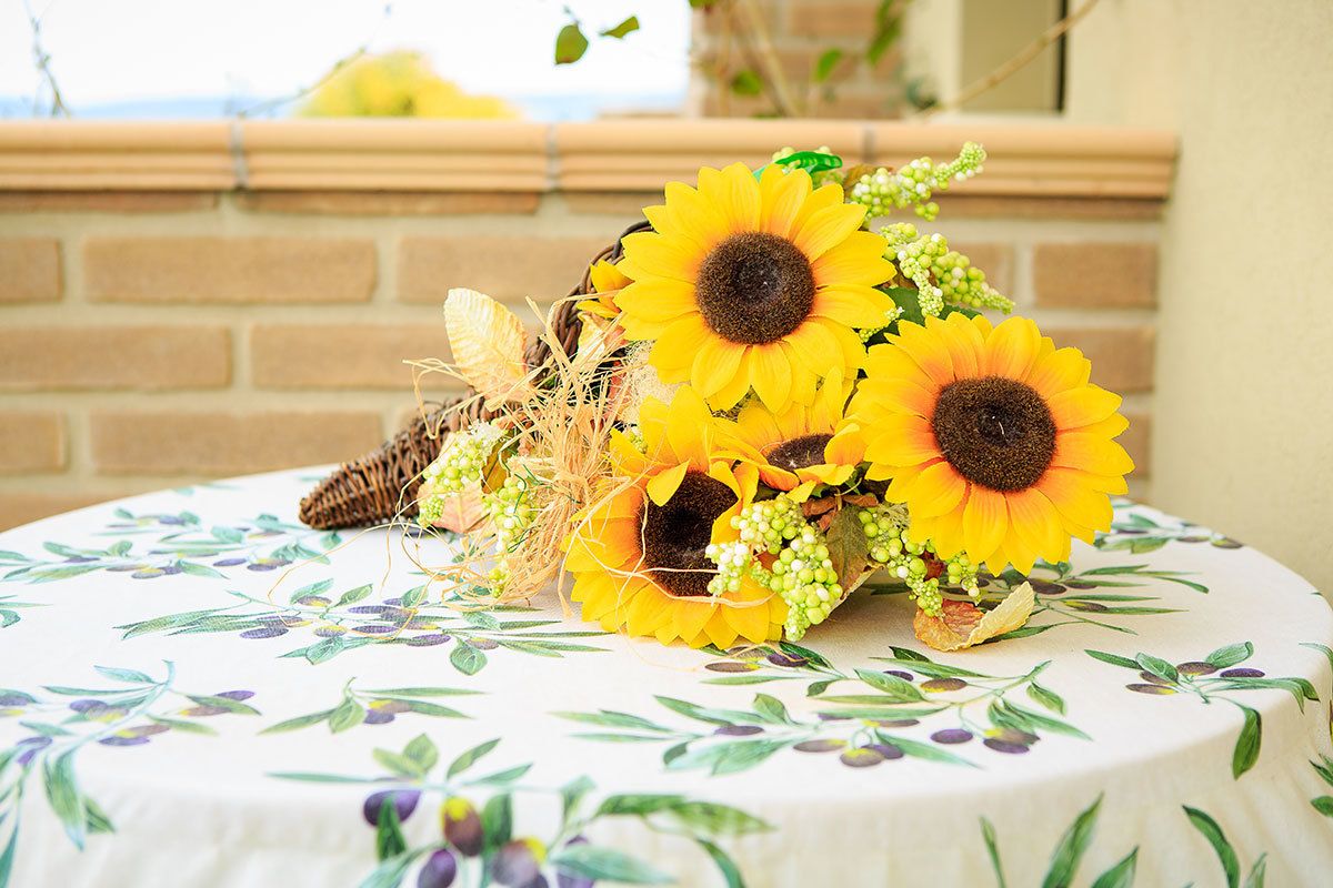 Una mesa redonda con mantel floral, una cesta de girasoles y plantas secas.