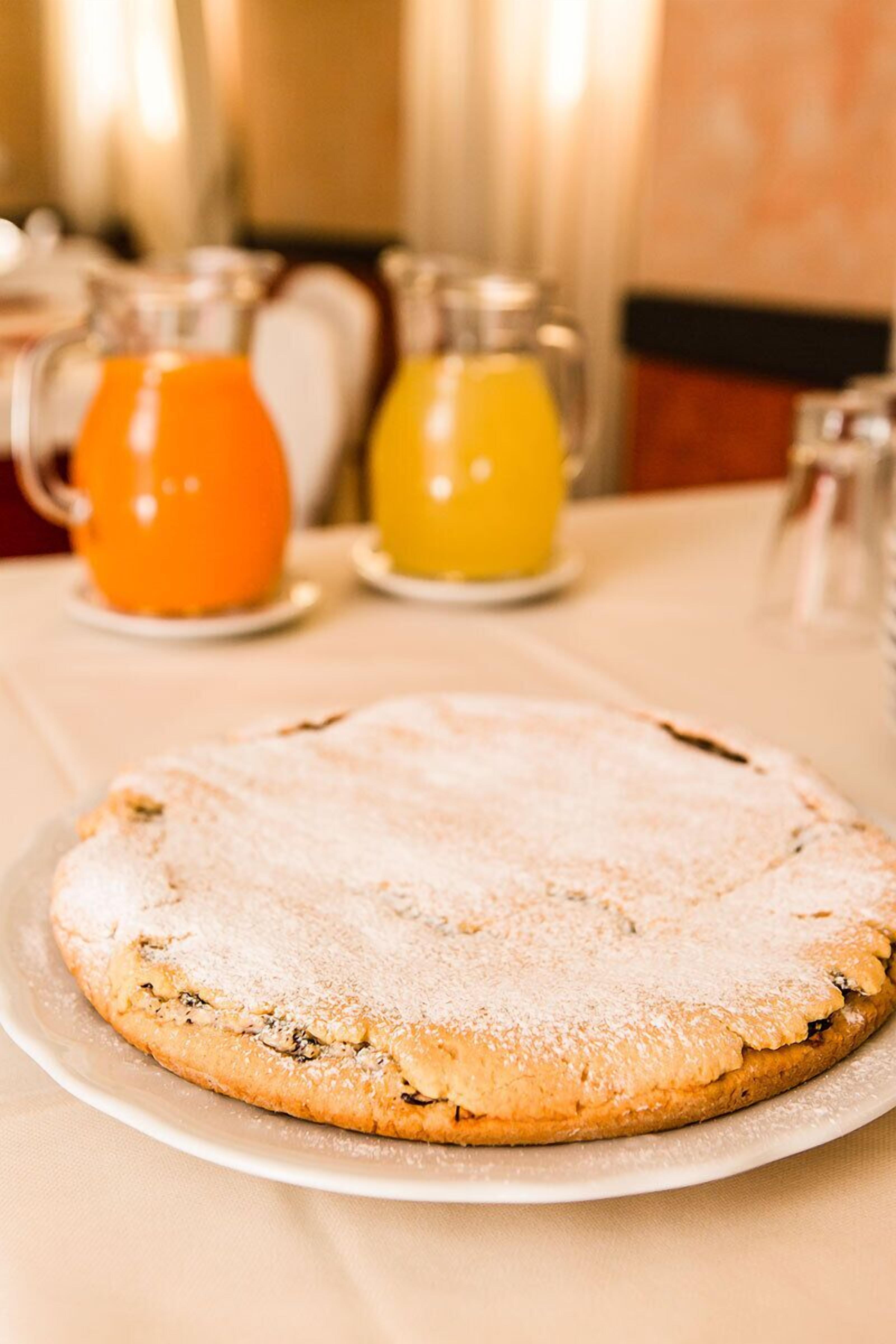 Un dolce rotondo su un piatto, con due caraffe di bevande arancioni e gialle sullo sfondo.