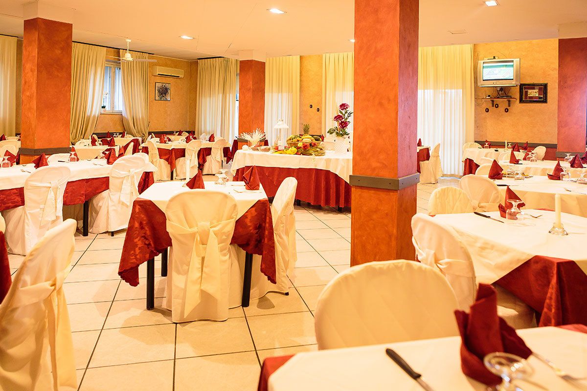A banquet hall with multiple round tables, each set with white tablecloths and red napkins.