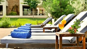 A poolside area with lounge chairs, towels, and a table with a drink and fruit. - Sani Polyastron Hotel & Spa (Kassandra)