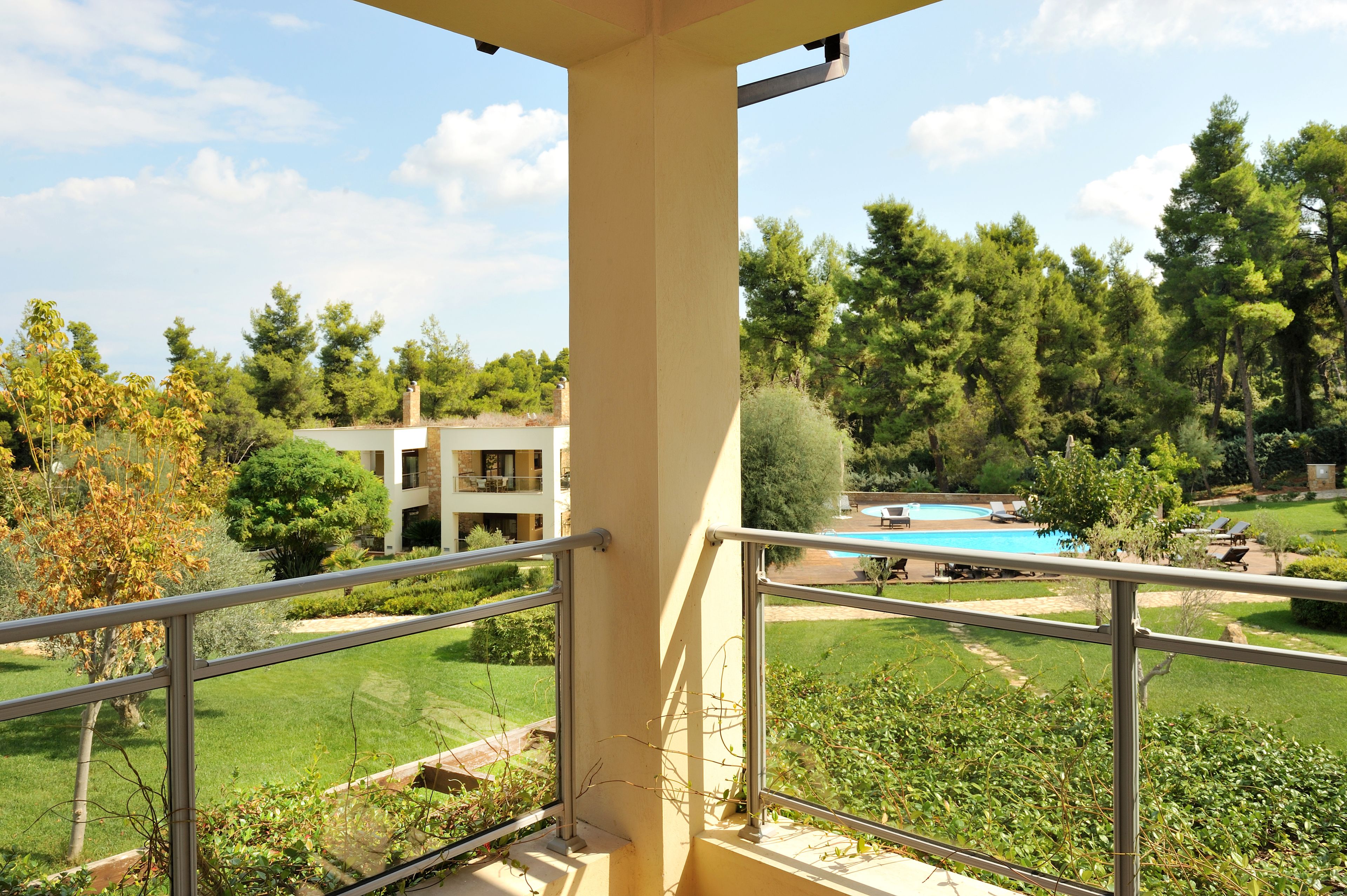 Un balcón con vista a una piscina, abundante vegetación y un edificio al fondo.