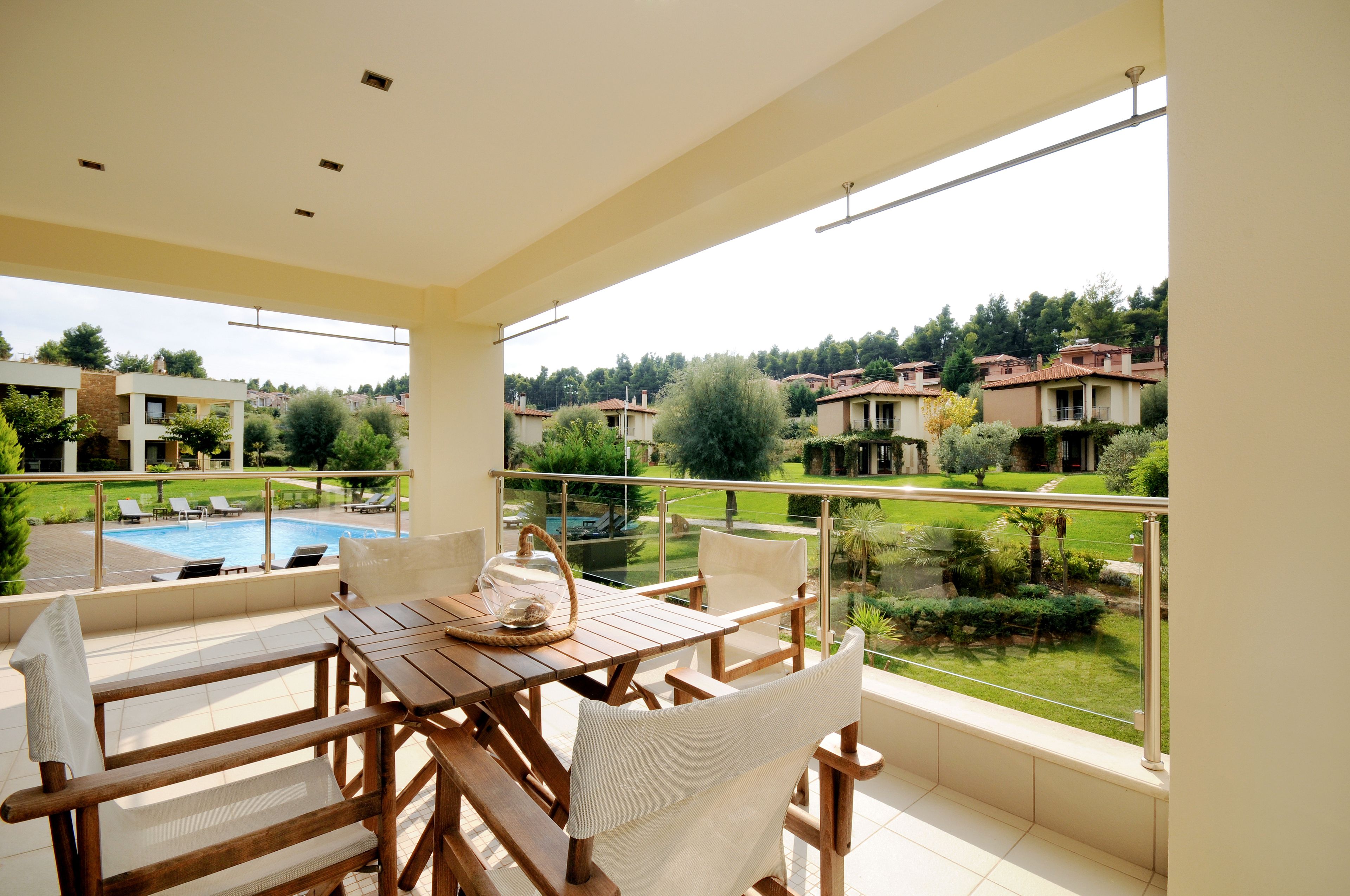 Un balcón con mesa y sillas de madera, con vistas a una piscina y una zona residencial.