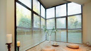 A room with large windows, a candle, a vase with plants, and two woven poufs on a wooden floor. - Sani Polyastron Hotel & Spa (Kassandra)