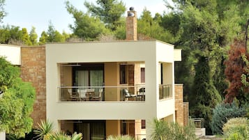 A modern two-story building with a balcony, surrounded by lush greenery and a stone pathway.