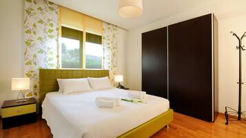 A neatly made bed with white linens, a green headboard, and two bedside lamps. There is a large wardrobe and a coat rack to the right.