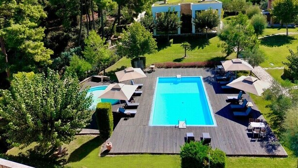 A large rectangular swimming pool surrounded by lounge chairs and umbrellas, with a wooden deck and lush greenery in the background. - Sani Polyastron Hotel & Spa (Kassandra)