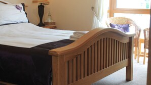 A neatly made bed with a wooden headboard, a bedside lamp, and a wicker chair by the window. - Quay Rest  (Rooskey)