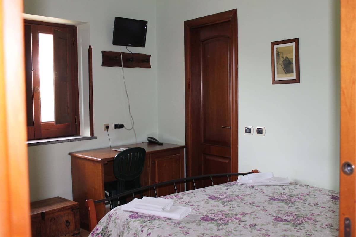 Une chambre à coucher comprenant un lit, un bureau, une chaise, un téléviseur fixé au mur et une porte.