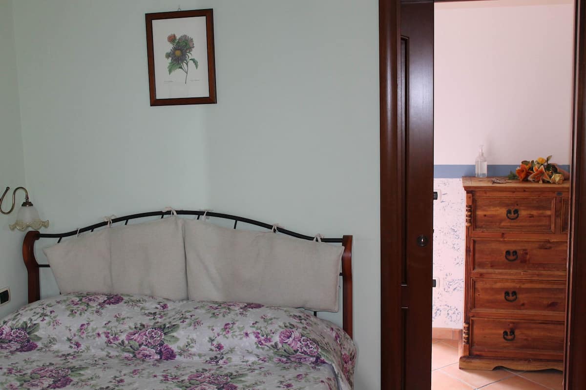 Une chambre à coucher avec un lit, une commode en bois et une illustration botanique encadrée accrochée au mur.
