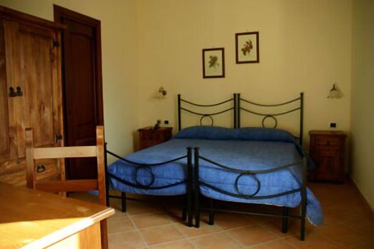 Une chambre à coucher avec un lit en métal, une armoire en bois et deux tables de chevet avec des lampes.